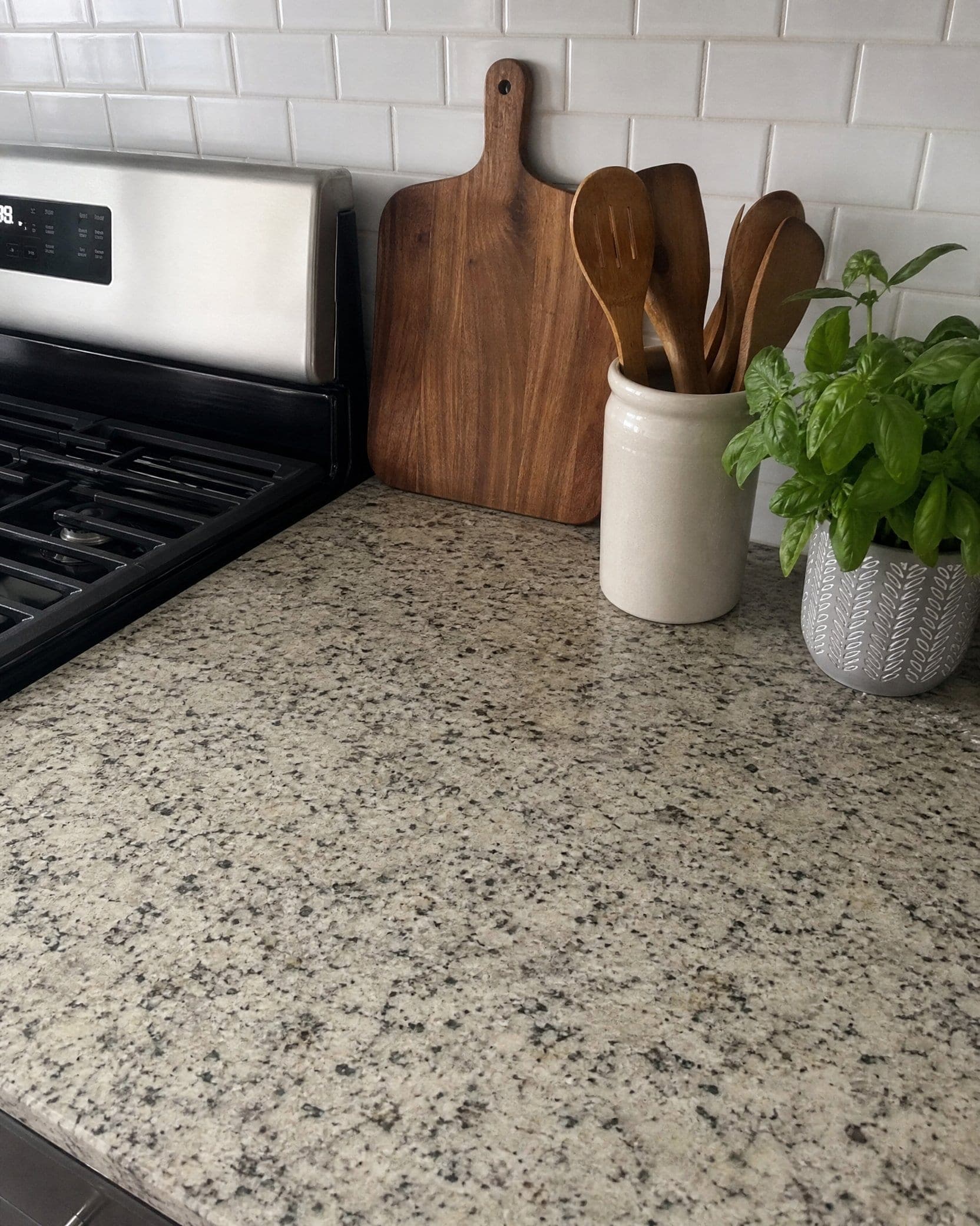 A clean kitchen counter with a cutting board, utensils, and a fresh basil plant